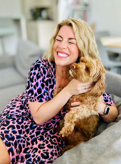 Woman in a pink leopard print dress holding a small brown dog indoors.