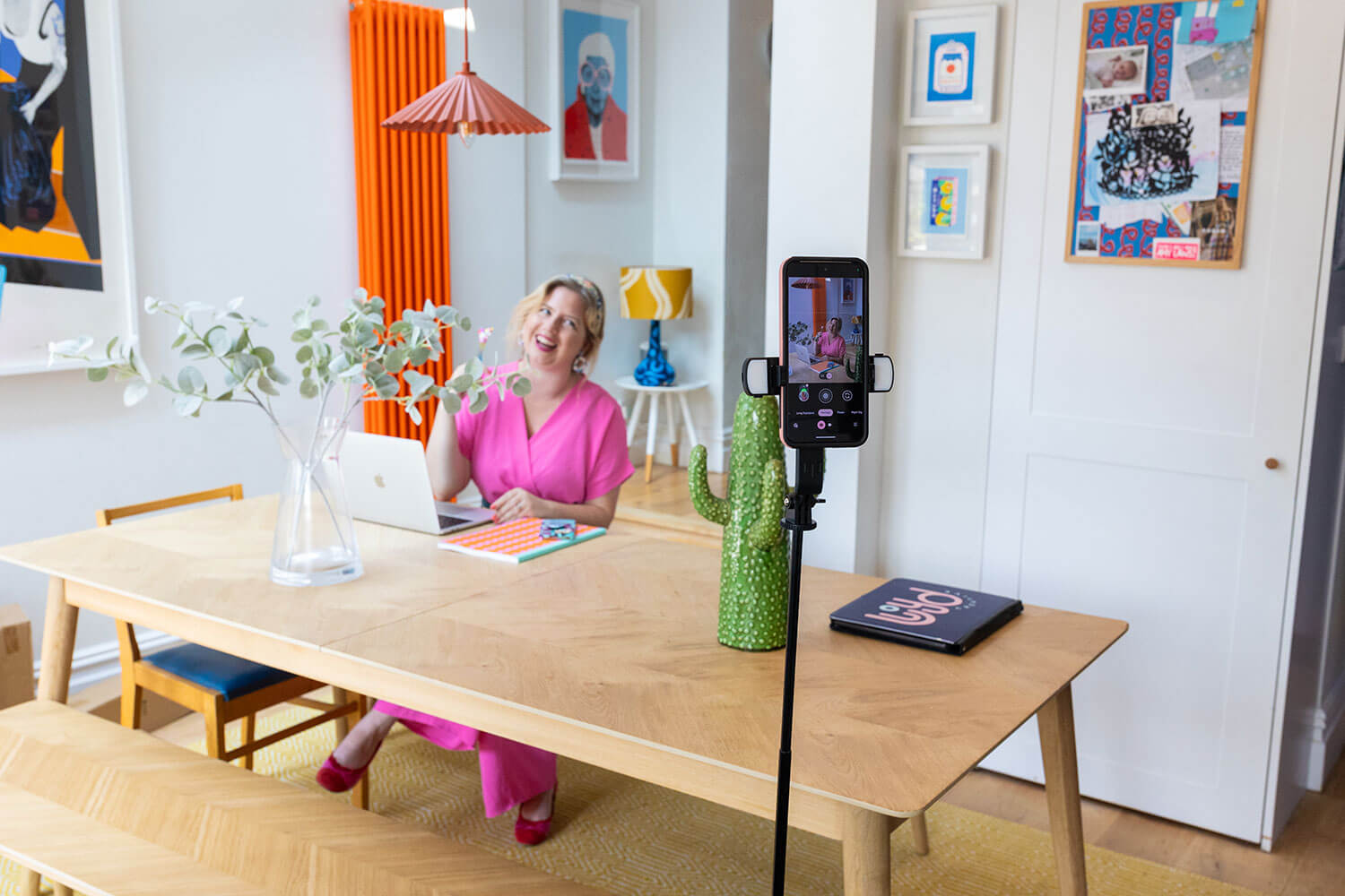 Woman in a pink dress sitting at a table with a laptop, taking a selfie self portrait