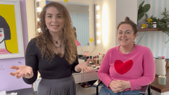 Two women sitting in a room with a mirror and makeup items.